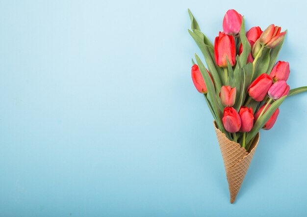 Red  beautiful tulips in an ice cream waffle cone with card Womans Day on a concrete background. Conceptual idea of a flower gift. Spring mood