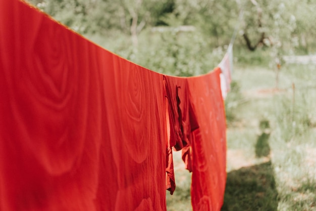 Red bed linen is dried on a clothesline on the street in courtyard of village household cottage house summer freshness and laundry day chore homework and hanging the laundry to dry on a rope