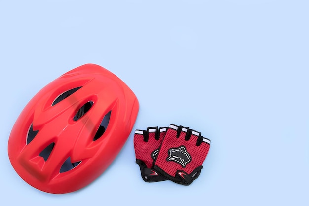 Red bicycle helmet and bicycle gloves on blue background with copy space