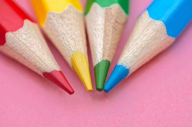 Red blue green and yellow pencils on a pink surface Close up