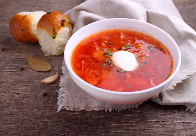 Red borscht soup in white bowl with sour cream and parsley