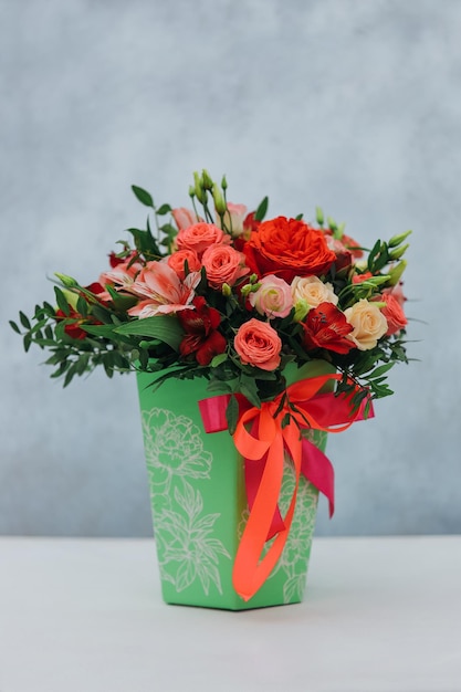 Red bouquet of rose alstroemeria and eustoma in a green paper gift box on a gray background