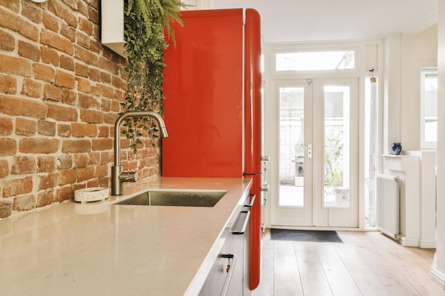 a red brick wall in a kitchen with white counter tops and an open door that leads to the dining area