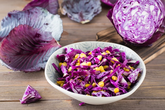 Red cabbage salad with corn grains in a plate on a wooden table