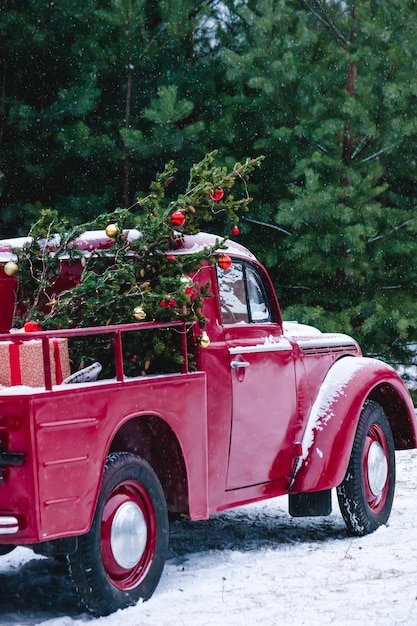 A red car with Christmas decorations and a Christmas tree is standing in a winter forest Festive New Year concept