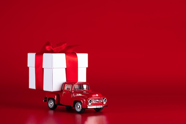 Red car with a gift box on a red background concept  delivery of gifts for the holidays valentines d...