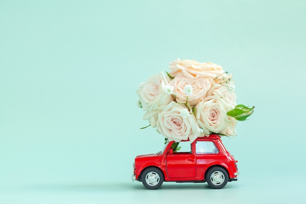 Photo red car with a roses flowers on the roof on blue background. happy valentine's day, mother's day, march 8, world women's day holiday card concept, flower delivery.