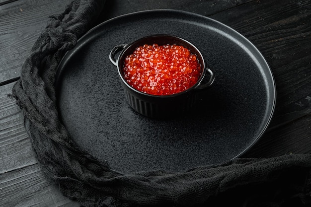 Red caviar black bowl on black wooden table background