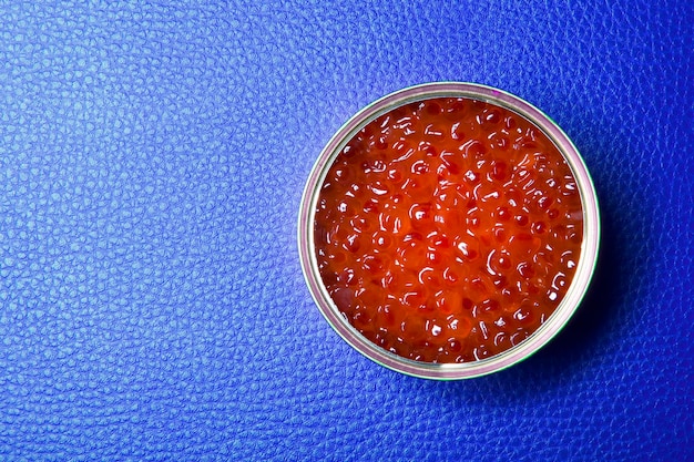 Red caviar in the open tin can on a dark blue background