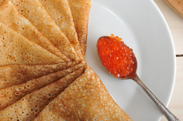 Red caviar in the spoon and pancakes in plate