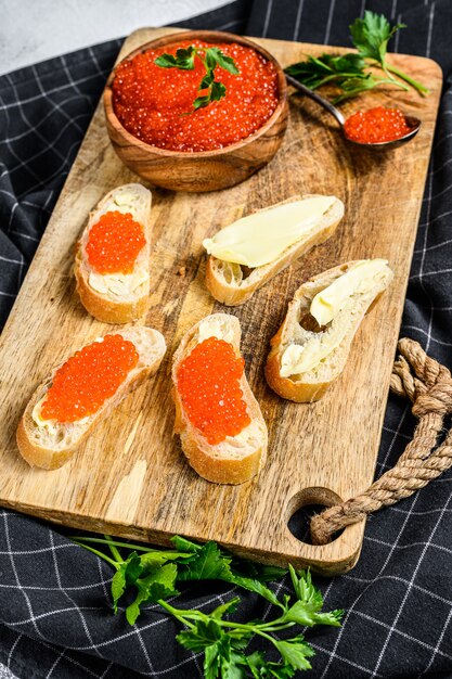 Red caviar in wooden bowl and Sandwiches on cutting board. Gray background. 