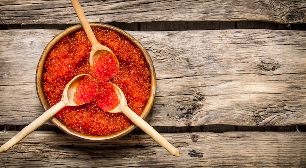 Red caviar in wooden cups with spoons. On a wooden table. Free space for text . Top view