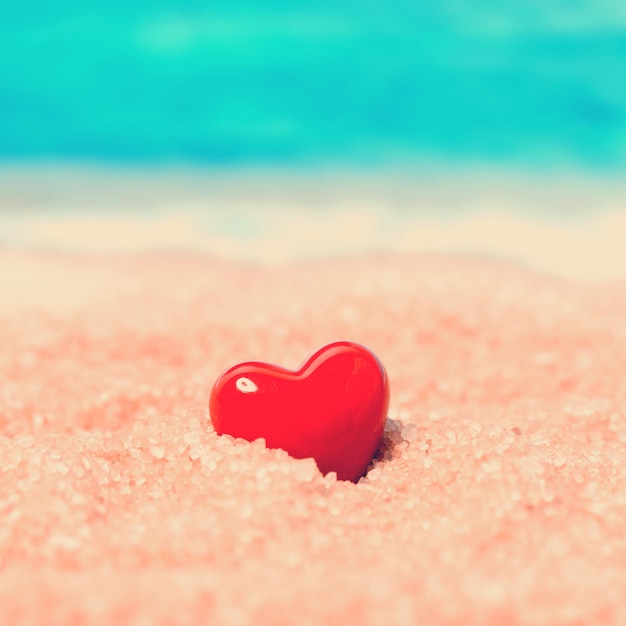 Red ceramic heart in the sand on the background of beach and sea Toned