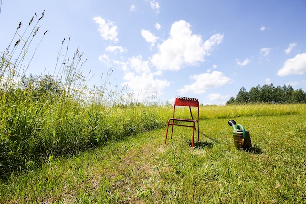 Red chair and watering can on mown green summer meadow in countryside.