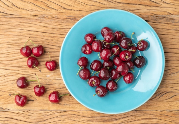 Red cherries on a blue plate over wooden table