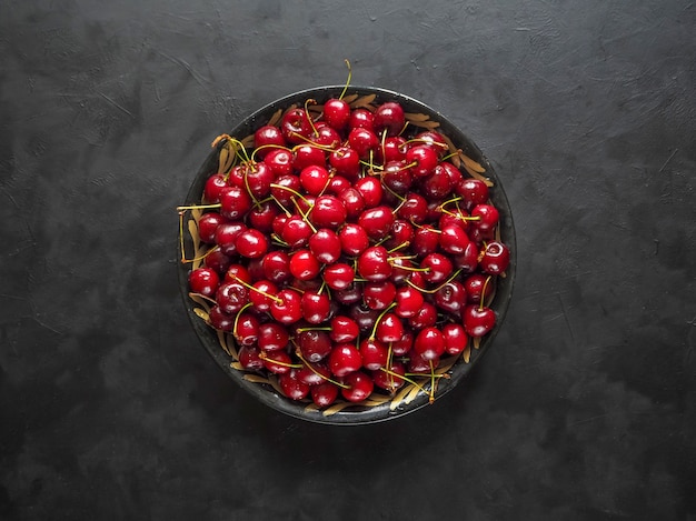 Red cherries in a plate on a black table. Top view. Copy space