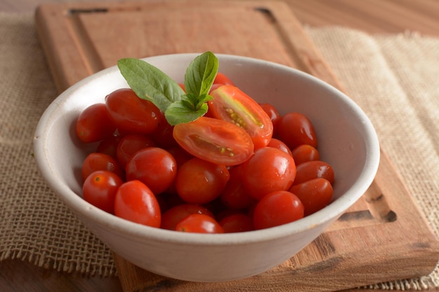 Red cherry tomatoes in a white bowl on a wooden table