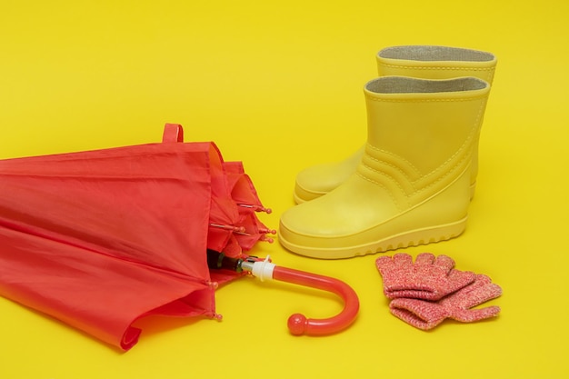 Red children's umbrella boots and gloves on a yellow background with copy space