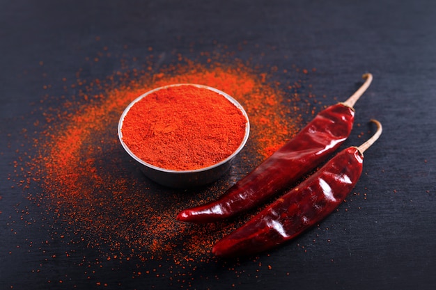 Red Chili pepper flakes and chili powder burst on black background