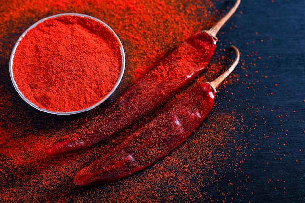 Red Chili pepper flakes and chili powder burst on black background