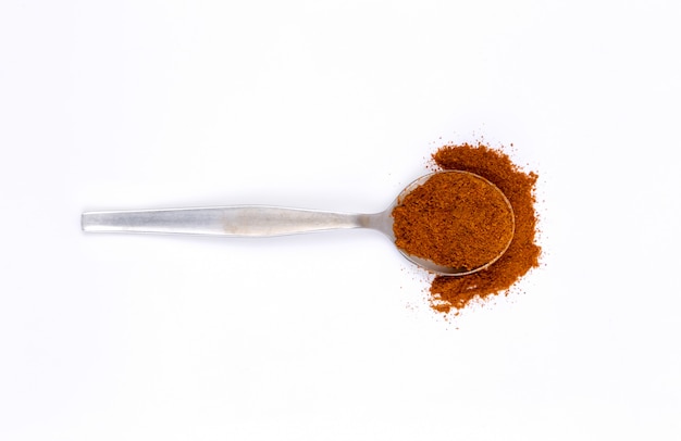 Red chili powder in metal spoon on white 