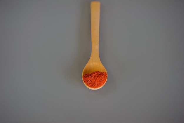 Red chili powder or paprika in a wooden bowl on a dark background, close-up. Cooking ingredients, flavor.