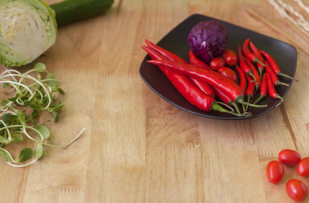 Red chilli with tomato and purple cabbage on black dish, wooden background