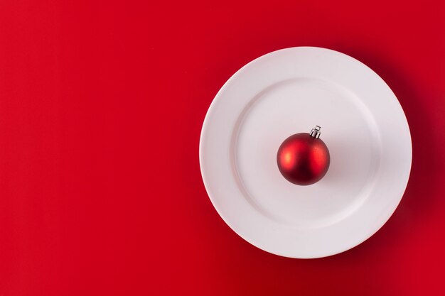 Red Christmas ball on white plate. Christmas dinner concept.