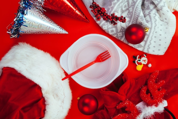 Red Christmas decoration with white plastic plate and red fork. Concept of charitable aid to the poor and homeless on the New Year.