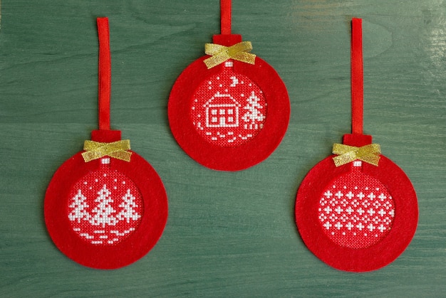 Red Christmas tree decoration made of felt with embroidered ornament on a green background