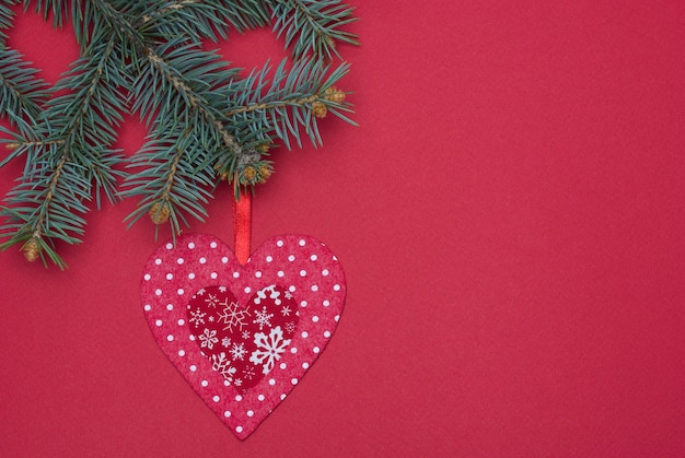 Red Christmas tree toy made of handmade felt hangs on a Christmas tree on a red background.