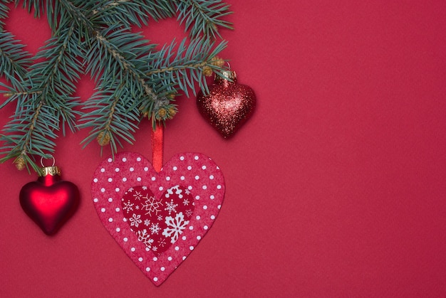 Red Christmas tree toy made of handmade felt hangs on a Christmas tree on a red background.