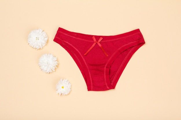 Red cotton panties with flower buds on beige background. Woman underwear set. Top view.