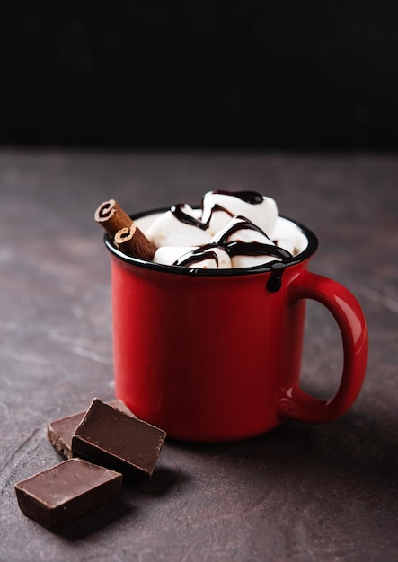 Red cup of aroma hot chocolate with marshmallows and cinnamon on a brown background Concept cozy drink Front view and copy space