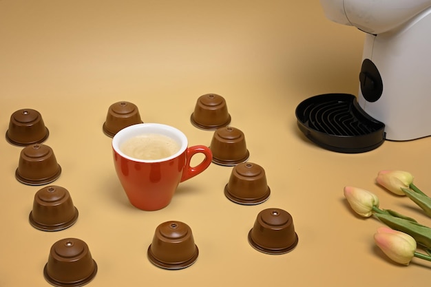 Red cup, coffee capsules and coffee machine on beige background.