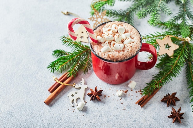 Red cup of hot cocoa with marshmallows and candy canes on with christmas tree