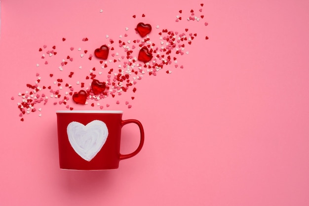 Red cup mug with with painted heart, sugar and chocolate hearts on pink table. Flat lay composition. Valentines Day concept. Top view, copy space.