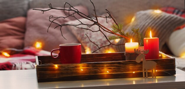 Red cup of tea on tray with burning candles near sofa with pillows