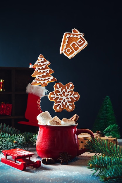 Red cup with marshmallows and cinnamon and flying Christmas gingerbread cookies