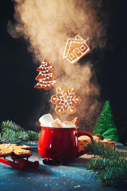 Red cup with marshmallows and cinnamon and flying Christmas gingerbread cookies