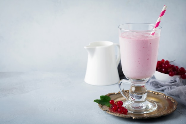 Red currant yoghurt smoothies, milkshake in a glass cup on a gray concrete surface. Selective focus. Copy space