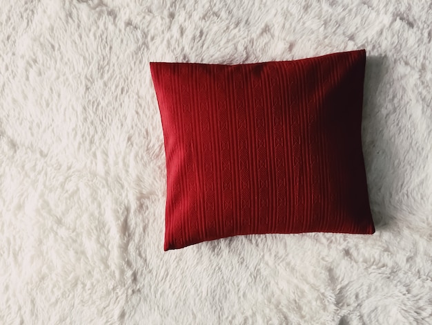 Red cushion throw pillow on white fluffy plaid blanket as flat lay