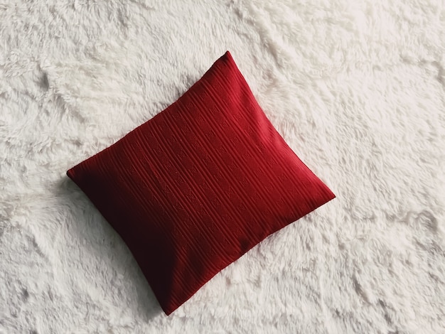 Red cushion throw pillow on white fluffy plaid blanket as flat lay