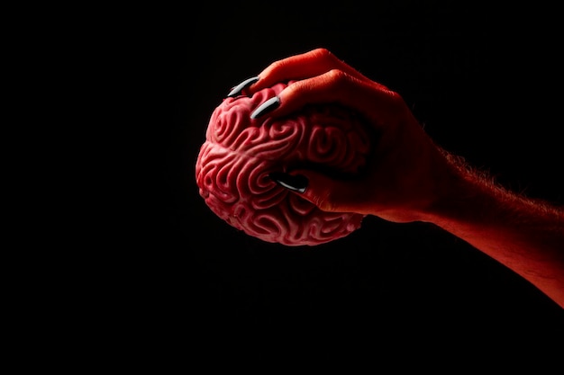 Photo red devil hand holding a human brain halloween concept