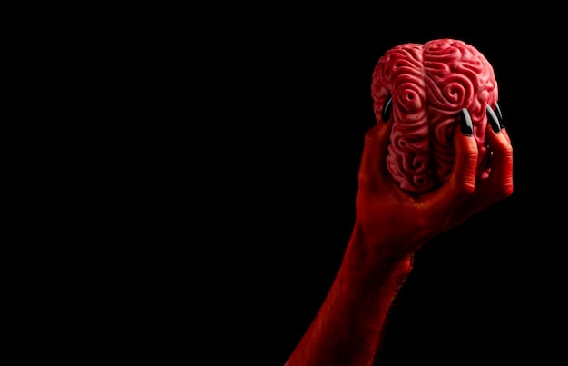 Red devil hand holding a human brain Halloween concept