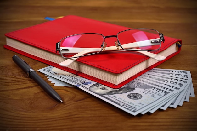 Red diary glasses pen and dollars