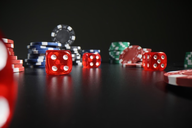 Red dice with digits and colorful poker chips scattered on dark table leaving reflections