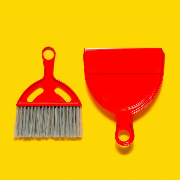 Red dustpan and brush lying on yellow