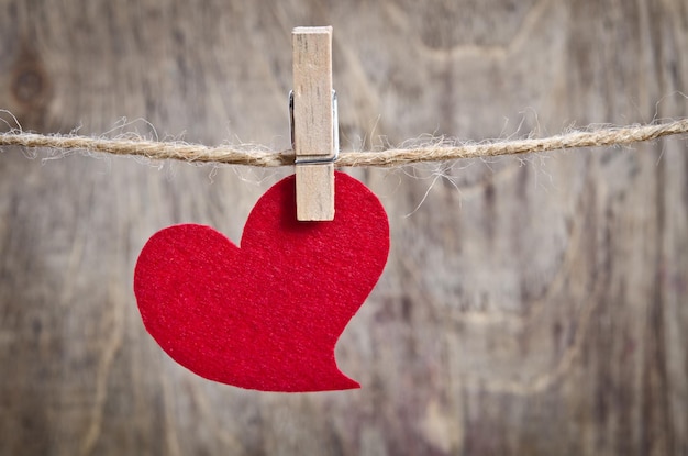 Red fabric heart hanging on the clothesline On old wood background