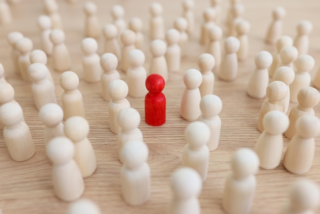 Red figure stands out of crowd with white figurines on wooden table surface leadership in